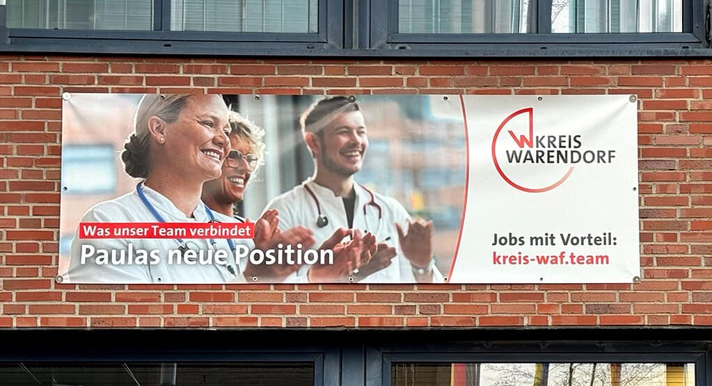 Banner der Arbeitgeberkampagne des Kreises Warendorf mit Mitarbeitenden aus dem Gesundheitswesen an einer Gebäudefassade.