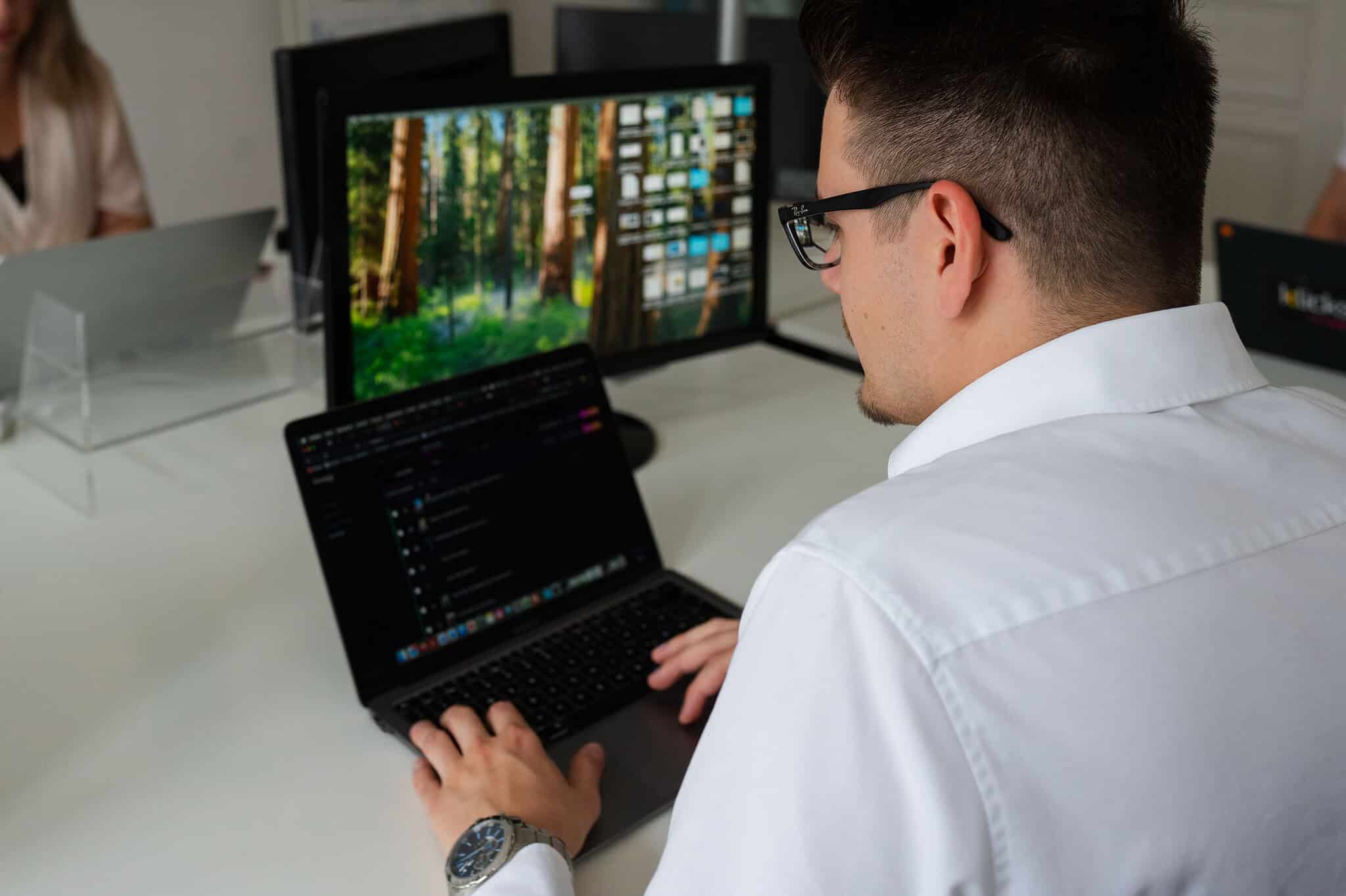 Mitarbeiter arbeitet konzentriert am Laptop und einem externen Monitor in einem modernen Büro.