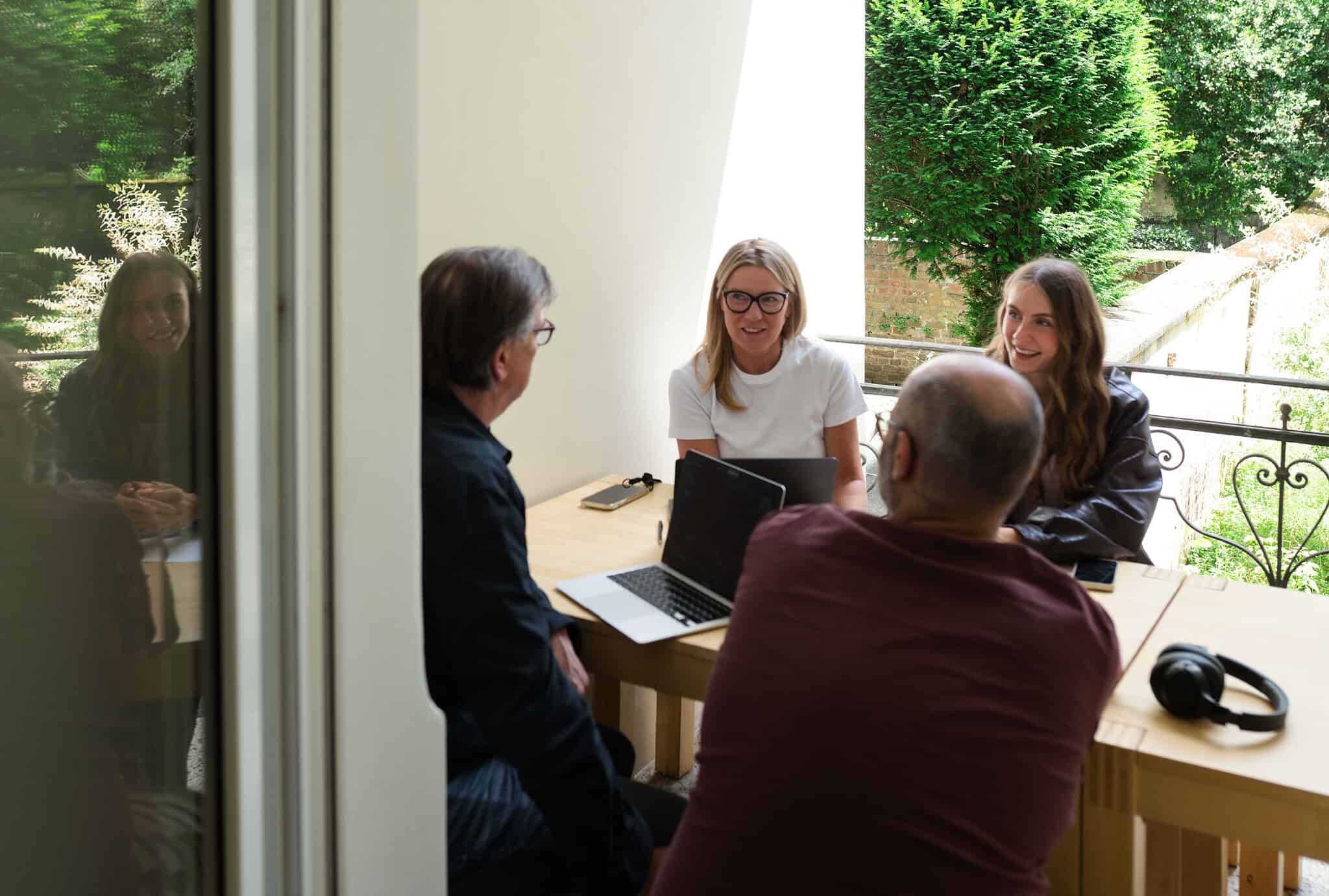 Vier Mitarbeitende bei einer gemeinsamen Besprechung mit Laptops an einem Tisch im Büro.