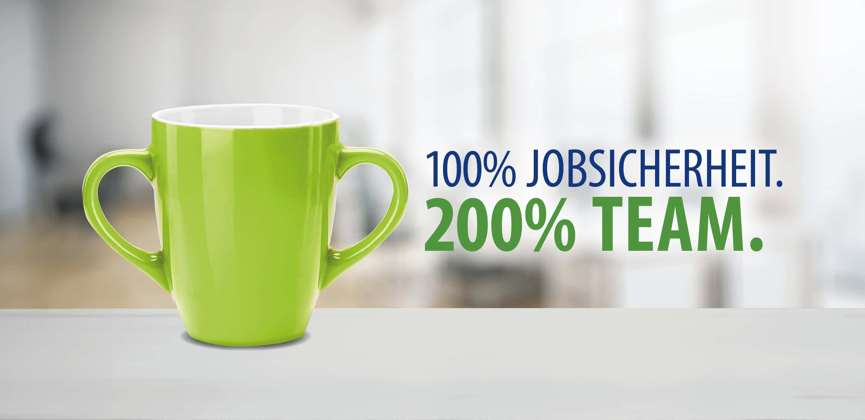 Grüne Tasse mit zwei Henkeln und dem Motiv „100 % Jobsicherheit. 200 % Team.“.